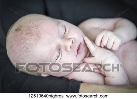Stock Photograph - A newborn baby boy with bare skin being held in a parent's arms; British Columbia, Canada. Fotosearch