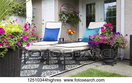 Stock Photograph - A patio at the back of a residence with two lounge chairs and pots of lush colourful flowers; Surrey, British Columbia, Canada. Fotosearch