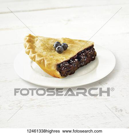 Stock Photograph - A piece of blueberry pie on a white plate with fresh blueberries garnishing the top. Fotosearch