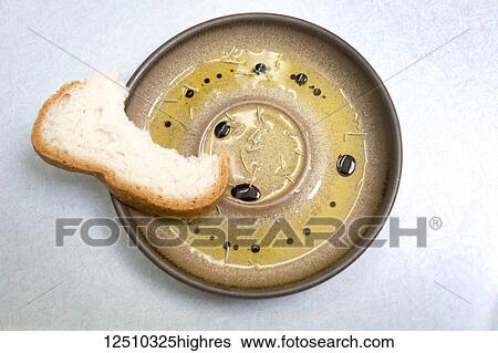 Stock Photograph - A piece of bread with bites out of it set on a plate with olive oil.. balsamic vinegar and rosemary. Fotosearch