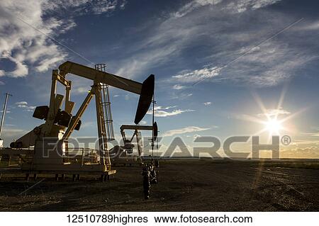 A pumpjack backlit by the setting sun on the Alberta Prairies with blue sky and cloud, West of Airdrie; Alberta, Canada View Large Photo Image Stock Photograph - A pumpjack backlit by the setting sun on the Alberta Prairies with blue sky and cloud, West of Airdrie; Alberta, Canada. Fotosearch