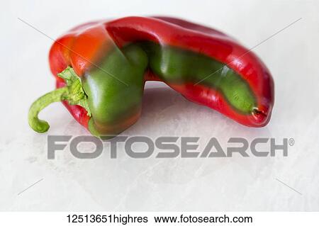 Stock Photograph - A red bell pepper in a unique shape and with a green stripe laying on a marble counter. Fotosearch