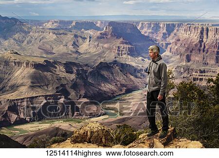 Stock Photograph - A senior man hiking in the Grand Canyon and standing on a ridge looking out over the landscape; Arizona, United States of America. Fotosearch