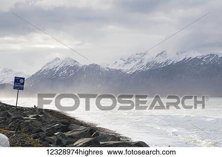 Stock Photograph - A sign to adopt a highway in the mist along the water; Alaska, United States of America. Fotosearch
