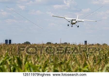 Stock Photograph - A small plane flies low over a farm field; Manitoba, Canada. Fotosearch