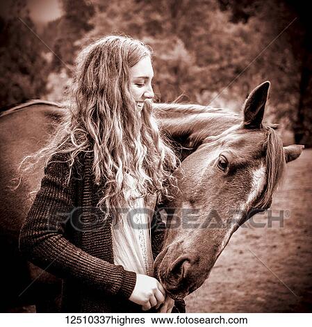 Stock Photograph - A teenage girl and her horse nibbling at her hands; British Columbia, Canada. Fotosearch