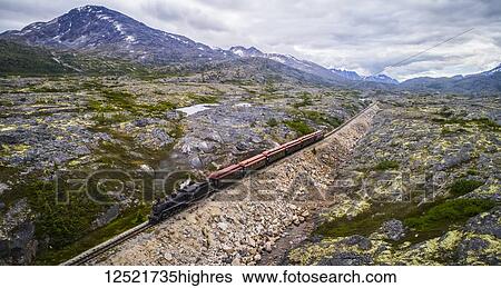 Stock Photograph - A train runs through the barren landscape on its way to Carcross; Yukon Territory, Canada. Fotosearch