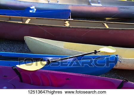Stock Photograph - A variety of coloured canoes and kayaks on the shore with a paddle, Lakeside Camp; Whidbey Island, Washington, United States of America. Fotosearch