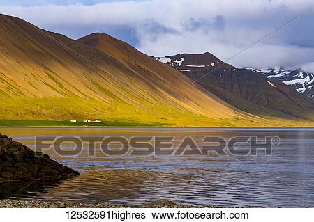 Stock Photograph - A vibrantly coloured hillside is enhanced by the setting sun and the colours reflect off of the ocean bay in Western Iceland; Iceland. Fotosearch
