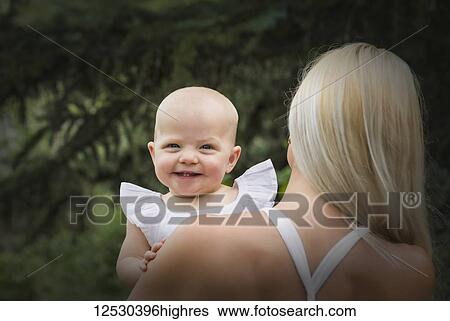 A view from behind of a beautiful young mom cuddling her baby daughter while enjoying quality time together outdoors in a park on a warm summer day; Edmonton, Alberta, Canada View Large Photo Image Stock Photograph - A view from behind of a beautiful young mom cuddling her baby daughter while enjoying quality time together outdoors in a park on a warm summer day; Edmonton, Alberta, Canada. Fotosearch