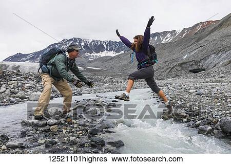 A wife jumps to her husband across an icy stream while hiking near Gulkana Glacier; Alaska, United States of America View Large Photo Image Stock Photograph - A wife jumps to her husband across an icy stream while hiking near Gulkana Glacier; Alaska, United States of America. Fotosearch
