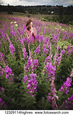 Stock Photograph - A woman in a prayerful pose in a meadow with fireweed (Chamaenerion angustifolium); Homer, Alaska, United States of America. Fotosearch