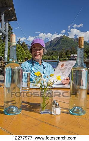 Stock Photo - A woman reads the menu at a outdoor table at the Saltry Restaurant in Halibut Cove, Southcentral Alaska, Summer.. Fotosearch