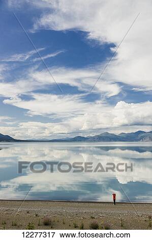 A woman stands at the shore of Kluane Lake with mountains and clouds reflecting in the calm waters of Kluane Lake, Yukon Territory, Canada, Summer View Large Photo Image Stock Photo - A woman stands at the shore of Kluane Lake with mountains and clouds reflecting in the calm waters of Kluane Lake, Yukon Territory, Canada, Summer. Fotosearch
