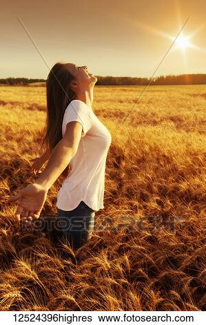 Stock Photograph - A woman stands in a wheat field with arms outstretched in surrender; Alberta, Canada. Fotosearch
