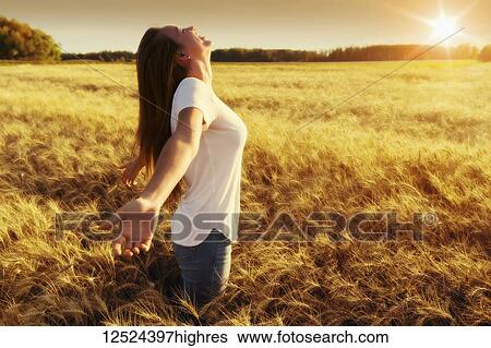 Stock Photograph - A woman stands in a wheat field with arms outstretched in surrender; Alberta, Canada. Fotosearch