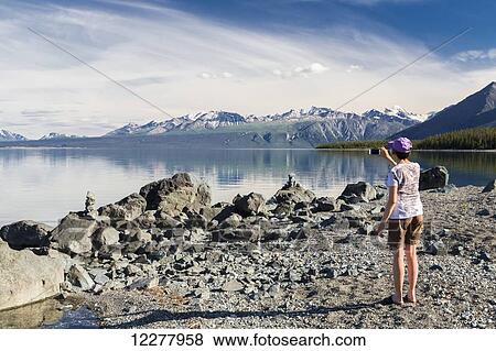 Stock Photo - A woman takes a photo of Kluane Lake with a smart phone, Yukon Territory, Canada, Summer.. Fotosearch