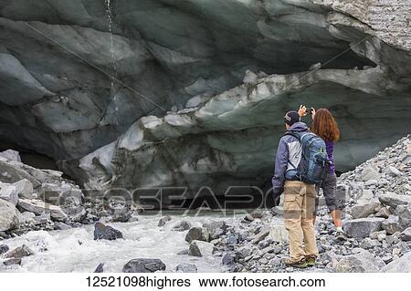 A woman takes a photograph of an ice cave with her cell phone while hiking to Gulkana Glacier with her husband; Alaska, United States of America View Large Photo Image Stock Photograph - A woman takes a photograph of an ice cave with her cell phone while hiking to Gulkana Glacier with her husband; Alaska, United States of America. Fotosearch
