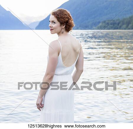 A woman with red hair and a white dress stands in the tranquil water of Alouette Lake on a summer evening; British Columbia, Canada View Large Photo Image Stock Photograph - A woman with red hair and a white dress stands in the tranquil water of Alouette Lake on a summer evening; British Columbia, Canada. Fotosearch