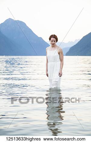 A woman with red hair and a white dress stands in the tranquil water of Alouette Lake on a summer evening; British Columbia, Canada View Large Photo Image Stock Photograph - A woman with red hair and a white dress stands in the tranquil water of Alouette Lake on a summer evening; British Columbia, Canada. Fotosearch