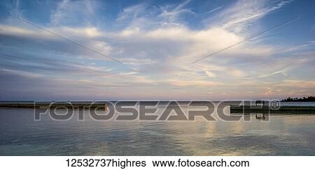 Stock Photograph - A wooden bench on a dock facing the coastline and open ocean at sunrise; Belize. Fotosearch
