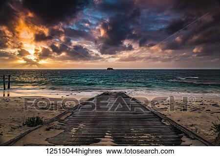 Stock Photograph - A wooden boardwalk on a beach leading to the turquoise water of Hamelin Bay at sunset; Western Australia, Australia. Fotosearch