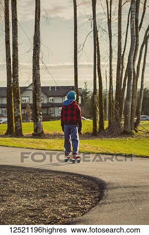 Stock Photograph - A young boy riding a skateboard on a trail in autumn; Langley, British Columbia, Canada. Fotosearch