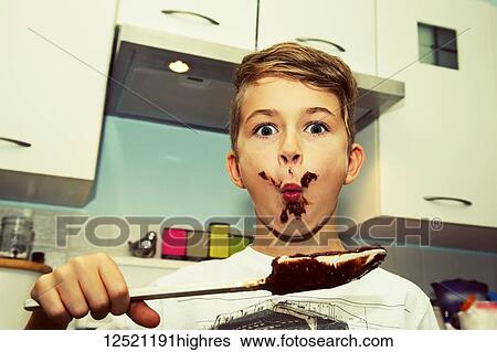 Stock Photograph - A young boy with a messy face licks the chocolate from the spatula after making fudge; Langley, British Columbia, Canada. Fotosearch