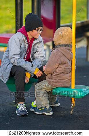 A young boy with his older brother sitting and talking at a playground; Langley, British Columbia, Canada View Large Photo Image Stock Photograph - A young boy with his older brother sitting and talking at a playground; Langley, British Columbia, Canada. Fotosearch