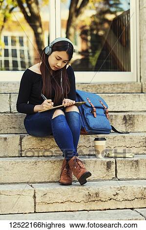 A young Chinese female university student sits on the steps listening to music using headphones and writes in notebook; Edmonton, Alberta, Canada View Large Photo Image Stock Photograph - A young Chinese female university student sits on the steps listening to music using headphones and writes in notebook; Edmonton, Alberta, Canada. Fotosearch