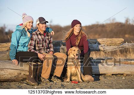 A young couple and a friend with a dog sit on a piece of driftwood on a beach looking out to the ocean at sunset; Anchorage, Alaska, United States of America View Large Photo Image Stock Photograph - A young couple and a friend with a dog sit on a piece of driftwood on a beach looking out to the ocean at sunset; Anchorage, Alaska, United States of America. Fotosearch