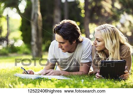 A young couple lays down studying outdoors on the grass on the university campus with a textbook and tablet and checking social media on a smart phone; Edmonton, Alberta, Canada View Large Photo Image Stock Photograph - A young couple lays down studying outdoors on the grass on the university campus with a textbook and tablet and checking social media on a smart phone; Edmonton, Alberta, Canada. Fotosearch