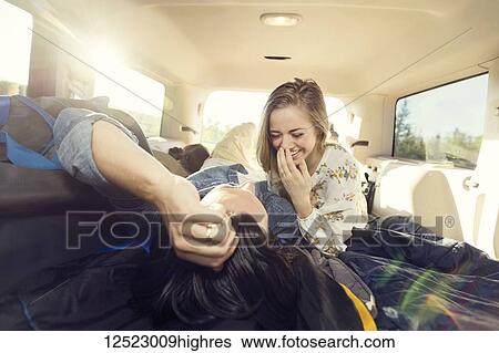 Stock Photograph - A young couple lays in the back of their vehicle during a road trip talking and laughing together; Edmonton, Alberta, Canada. Fotosearch