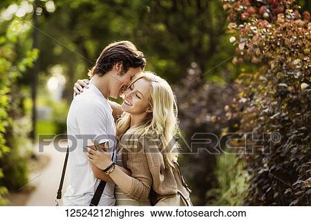 Stock Photograph - A young couple shares a romantic moment together in an embrace on a pathway on the university campus; Edmonton, Alberta, Canada. Fotosearch