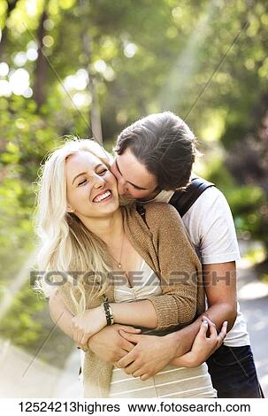 Stock Photograph - A young couple shares a romantic moment together in an embrace on a pathway on the university campus; Edmonton, Alberta, Canada. Fotosearch