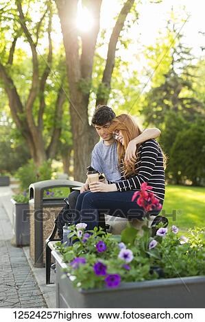 A young couple sitting together on a bench in a park and checking social media on a smart phone; Edmonton, Alberta, Canada View Large Photo Image Stock Photograph - A young couple sitting together on a bench in a park and checking social media on a smart phone; Edmonton, Alberta, Canada. Fotosearch