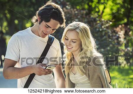 Stock Photograph - A young couple stand together on the university campus looking at a smart phone; Edmonton, Alberta, Canada. Fotosearch