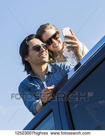 A young couple stand up through the sunroof of their vehicle and take a self-portrait with their cell phone; Edmonton, Alberta, Canada View Large Photo Image Stock Photograph - A young couple stand up through the sunroof of their vehicle and take a self-portrait with their cell phone; Edmonton, Alberta, Canada. Fotosearch