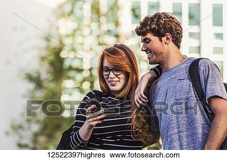 A young couple standing together and checking social media on a smart phone while walking through a university campus; Edmonton, Alberta, Canada View Large Photo Image Stock Photograph - A young couple standing together and checking social media on a smart phone while walking through a university campus; Edmonton, Alberta, Canada. Fotosearch