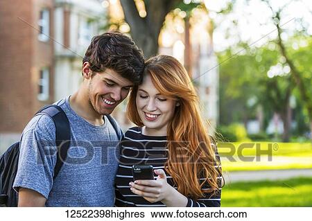 A young couple standing together and checking social media on a smart phone while walking through a university campus; Edmonton, Alberta, Canada View Large Photo Image Stock Photograph - A young couple standing together and checking social media on a smart phone while walking through a university campus; Edmonton, Alberta, Canada. Fotosearch