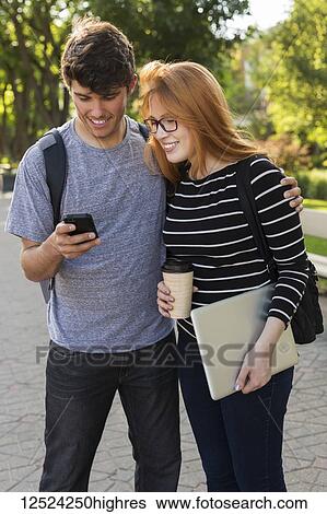 A young couple standing together and checking social media on a smart phone while walking through a university campus; Edmonton, Alberta, Canada View Large Photo Image Stock Photograph - A young couple standing together and checking social media on a smart phone while walking through a university campus; Edmonton, Alberta, Canada. Fotosearch