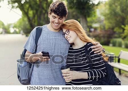 A young couple standing together and checking social media on a smart phone while walking through a university campus; Edmonton, Alberta, Canada View Large Photo Image Stock Photograph - A young couple standing together and checking social media on a smart phone while walking through a university campus; Edmonton, Alberta, Canada. Fotosearch