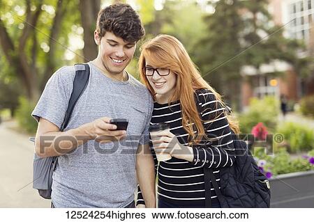 A young couple standing together and checking social media on a smart phone while walking through a university campus; Edmonton, Alberta, Canada View Large Photo Image Stock Photograph - A young couple standing together and checking social media on a smart phone while walking through a university campus; Edmonton, Alberta, Canada. Fotosearch