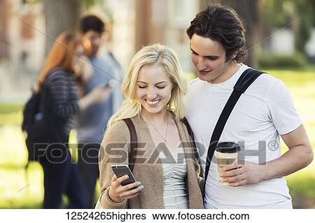 A young couple standing together and checking social media on a smart phone while walking through a university campus; Edmonton, Alberta, Canada View Large Photo Image Stock Photograph - A young couple standing together and checking social media on a smart phone while walking through a university campus; Edmonton, Alberta, Canada. Fotosearch