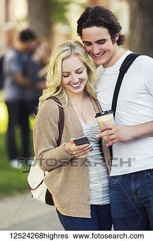 A young couple standing together and checking social media on a smart phone while walking through a university campus; Edmonton, Alberta, Canada View Large Photo Image Stock Photograph - A young couple standing together and checking social media on a smart phone while walking through a university campus; Edmonton, Alberta, Canada. Fotosearch