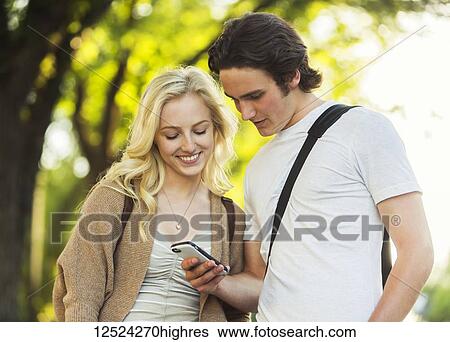 A young couple standing together and checking social media on a smart phone while walking through a university campus; Edmonton, Alberta, Canada View Large Photo Image Stock Photograph - A young couple standing together and checking social media on a smart phone while walking through a university campus; Edmonton, Alberta, Canada. Fotosearch