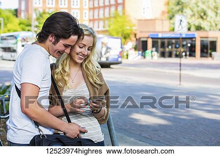 A young couple stands near a bus stop on the university campus looking at a smart phone; Edmonton, Alberta, Canada View Large Photo Image Stock Photograph - A young couple stands near a bus stop on the university campus looking at a smart phone; Edmonton, Alberta, Canada. Fotosearch