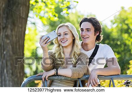 Stock Photograph - A young couple stands together at a bike rack on the university campus taking a self-portrait with a smart phone; Edmonton, Alberta, Canada. Fotosearch