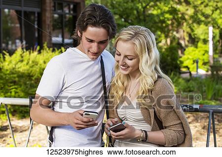 A young couple stands together on the university campus looking at their smart phones to show each other social media posts; Edmonton, Alberta, Canada View Large Photo Image Stock Photograph - A young couple stands together on the university campus looking at their smart phones to show each other social media posts; Edmonton, Alberta, Canada. Fotosearch