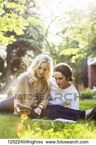 A young couple studying outdoors on the grass on the university campus and looking through a textbook while using a tablet; Edmonton, Alberta, Canada View Large Photo Image Stock Photograph - A young couple studying outdoors on the grass on the university campus and looking through a textbook while using a tablet; Edmonton, Alberta, Canada. Fotosearch